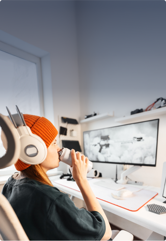 Girl sitting at a computer desk with a gaming set up drinking an energy drink