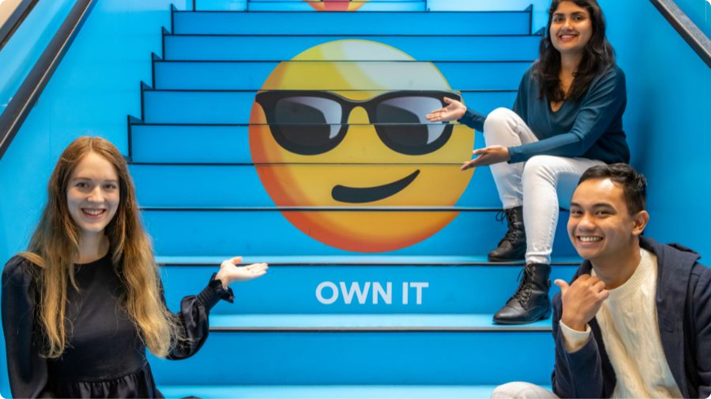 Photo of 2degrees staff members sitting on the stairs of the office showing our painted own it value and emoji on the staircase