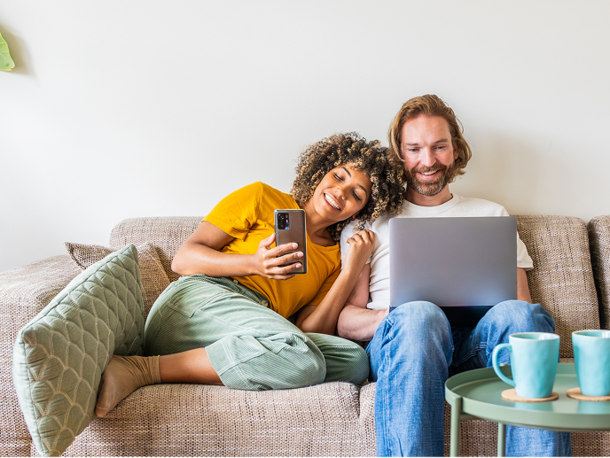 Image of a couple sitting on a couch with a woman on her phone and a man on his laptop